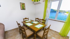 Uma área de refeições com mesa e cadeiras de madeira, um quadro na parede e uma janela com vista para a água.