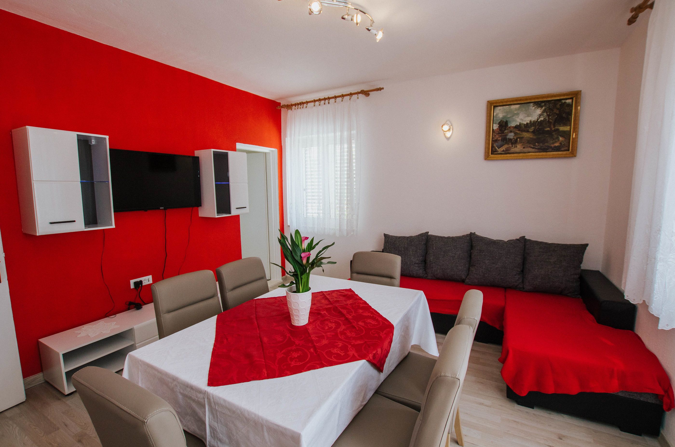 A modern room with a red accent wall, a white table with a red tablecloth, a sofa with red cushions, and a painting on the wall.