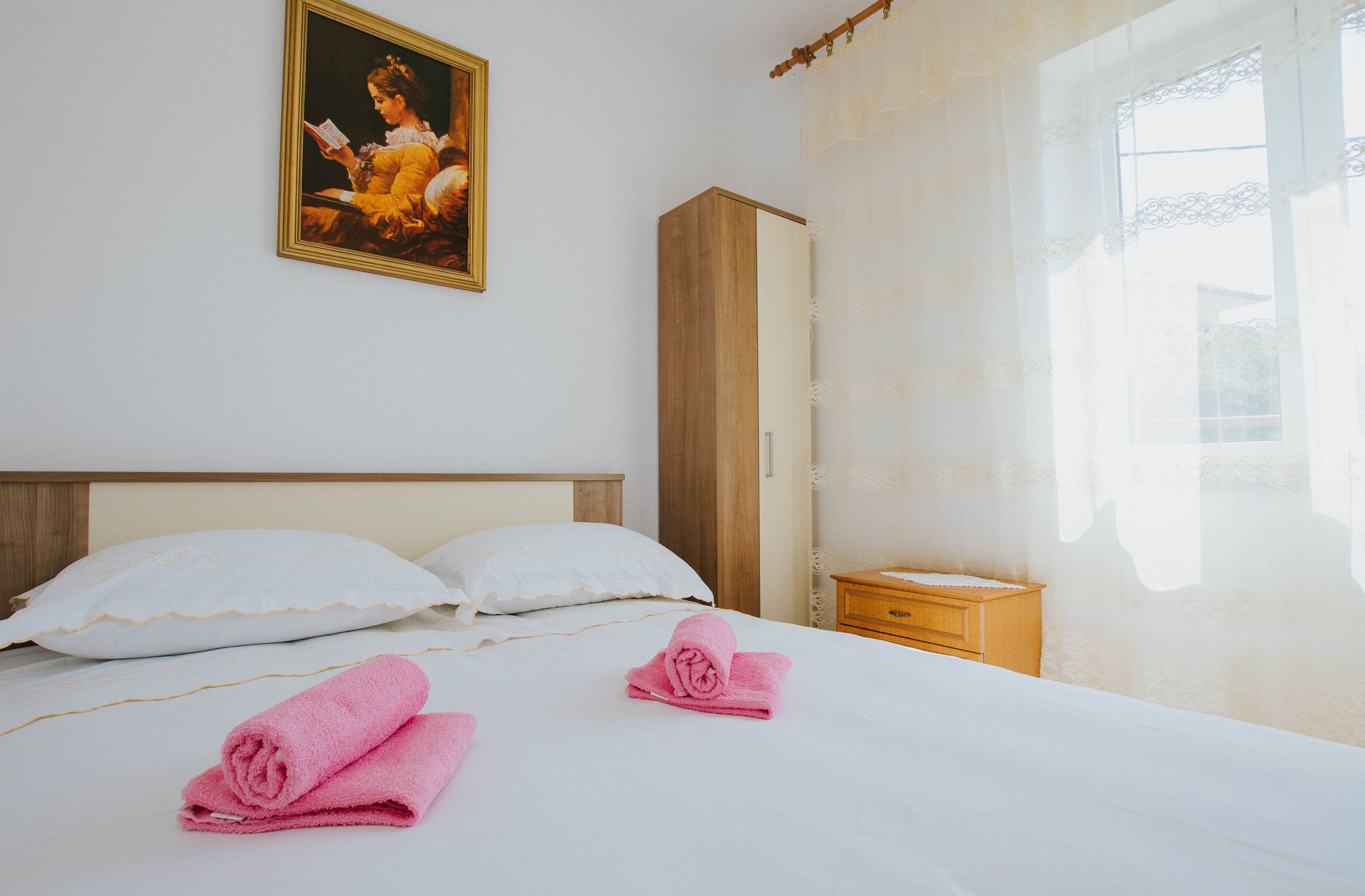 Habitación de hotel con cama, almohadas, mesita de noche, armario de madera y un cuadro en la pared.
