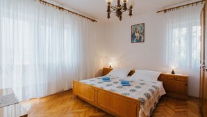 A bedroom with a wooden bed, white curtains, a chandelier, and a painting on the wall. - House Josipa (Okrug Gornji)