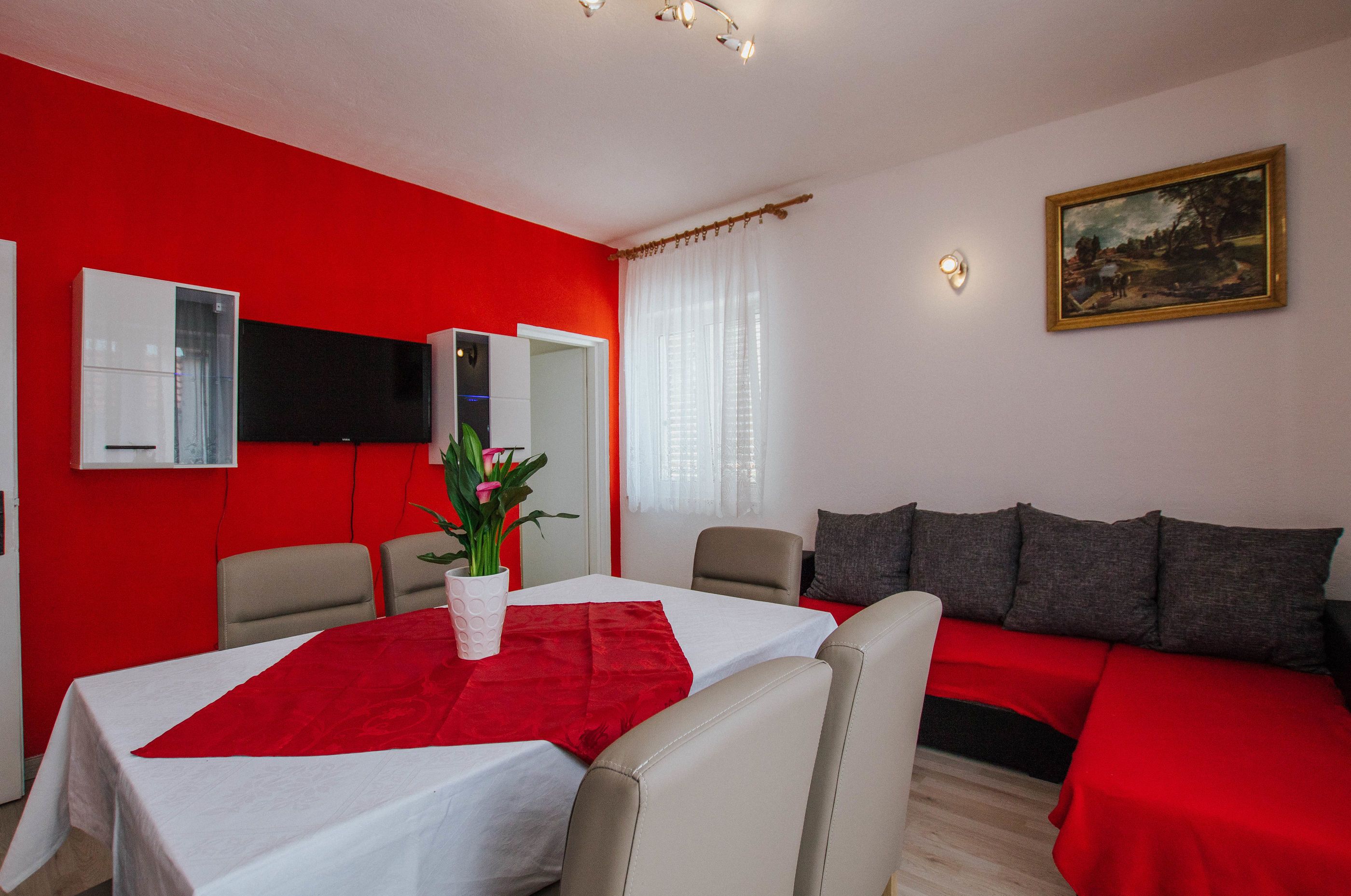 A room with a red wall, a white table with a red tablecloth, a sofa with red cushions, and a painting on the wall.