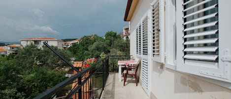 A balcony with a table and chairs, overlooking a garden and buildings.