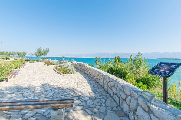 Un sentier pavé de pierres mène à un belvédère offrant une vue panoramique sur la mer et les montagnes.
