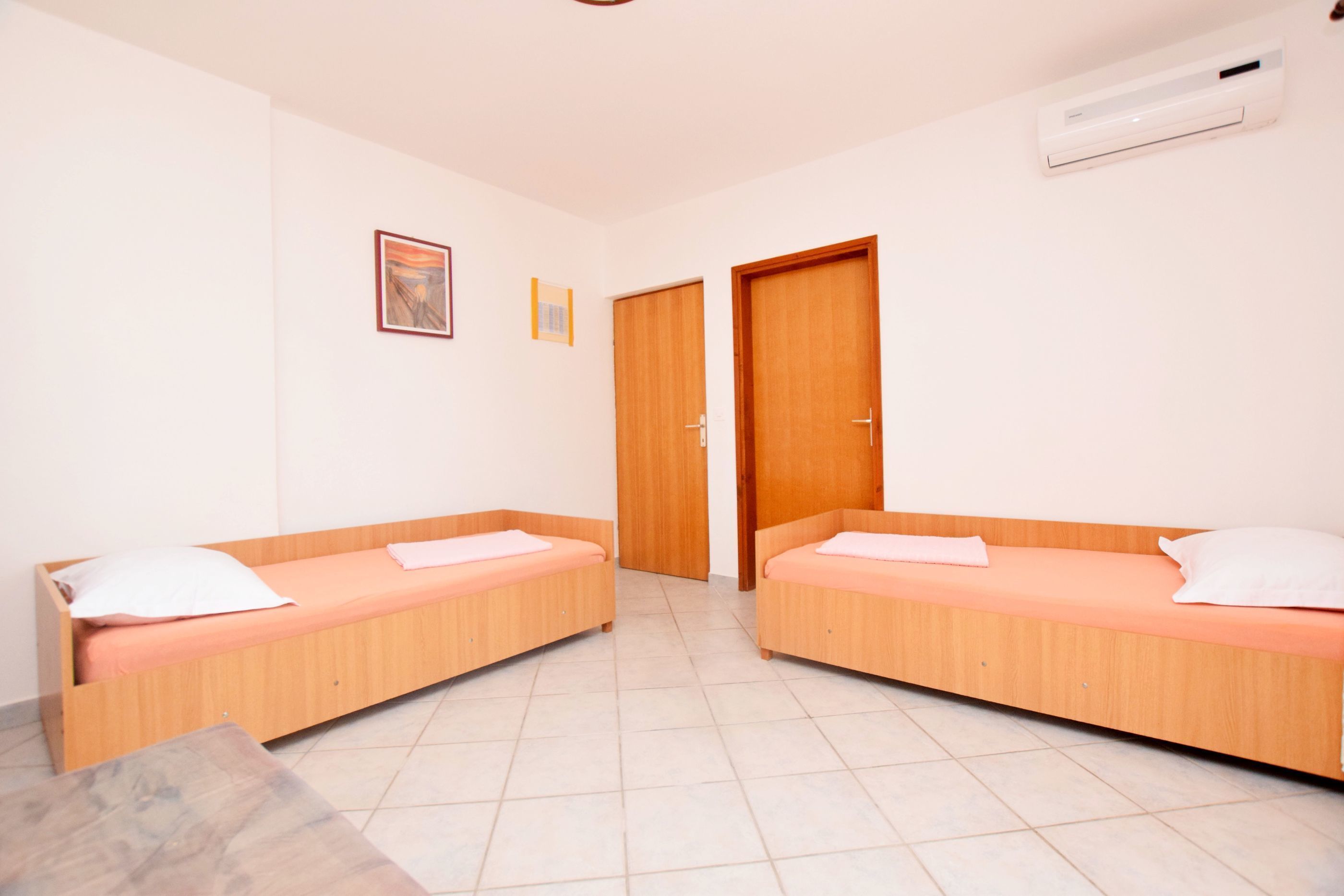 A room with two wooden beds, a small table, and a door.
