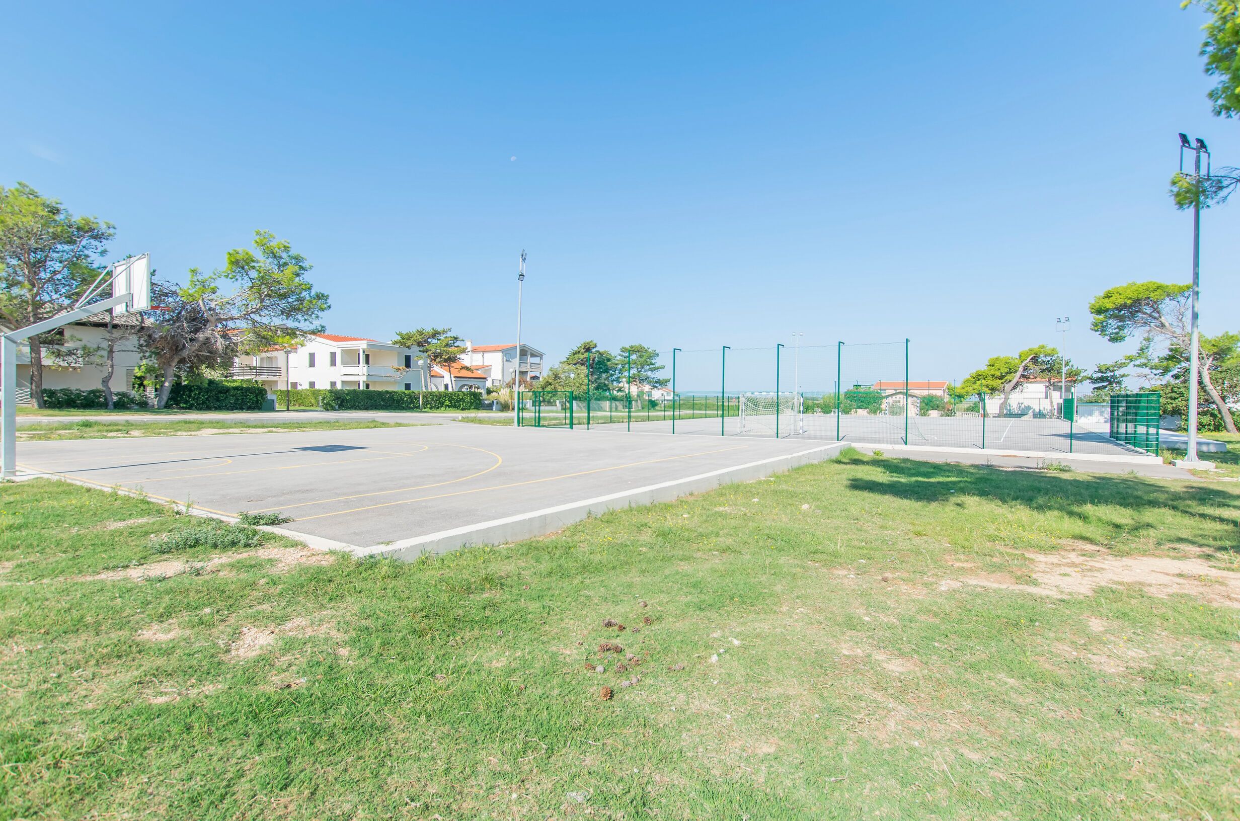 An outdoor basketball court with a net, surrounded by green fencing and trees.
