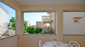 Un balcon avec une table et des chaises, une vue sur les bâtiments voisins et un sol carrelé.