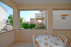 A balcony with a table and chairs, a view of neighboring buildings, and a tiled floor. - Apartments Ivan (Novalja)