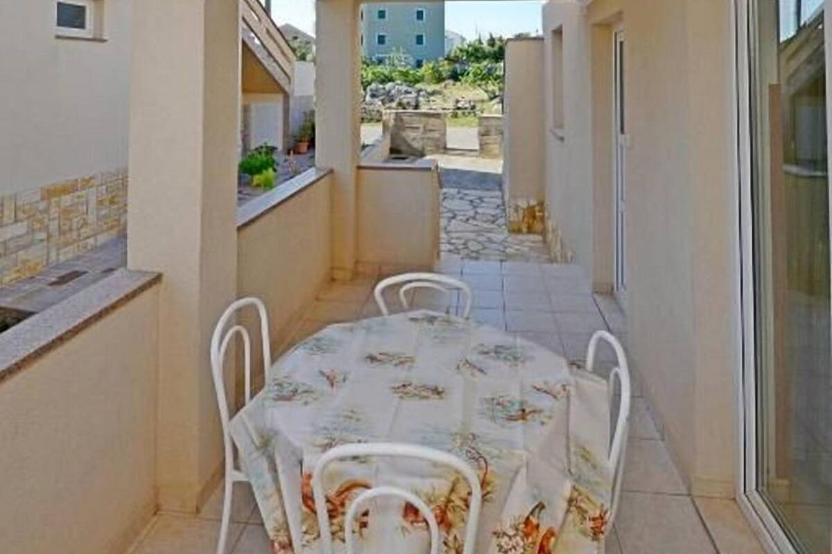 A covered outdoor dining area with a table and chairs, a small kitchen area, and a view of a building in the background.