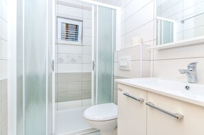 Een moderne badkamer met een douchecabine van glas, een toilet en een wastafel met een spiegel erboven.