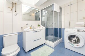 A modern bathroom with a toilet, sink, shower, and washing machine. - Apartments Sanja (Tribunj)