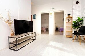 A modern living room with a flat-screen TV on a wooden console, a black chair, and a plant shelf. - Apartments Sanja (Tribunj)