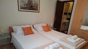 A double bed with white linens and orange pillows, a bedside table with a lamp, and a wooden wardrobe with a mirror. - Apartment Jolanka (Sukosan)