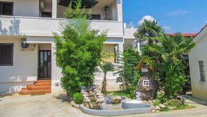 A two-story building with a courtyard featuring a small fountain, stone steps, and various plants. - Apartment Jolanka (Sukosan)