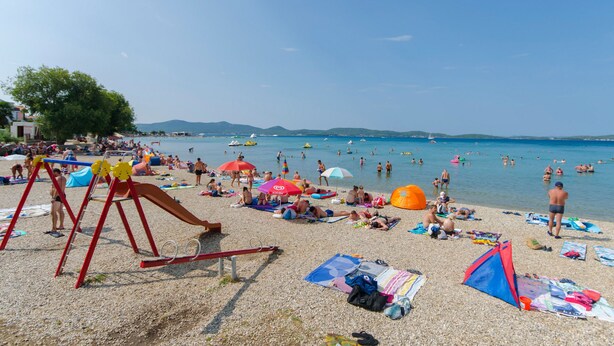 A beach with a playground, umbrellas, and people sunbathing. - Apartment Jolanka (Sukosan)
