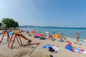 En strand med en lekplats, parasoller och folk som solar.