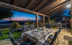 An outdoor patio with a table set for dining, surrounded by chairs, and a stone fireplace in the background.