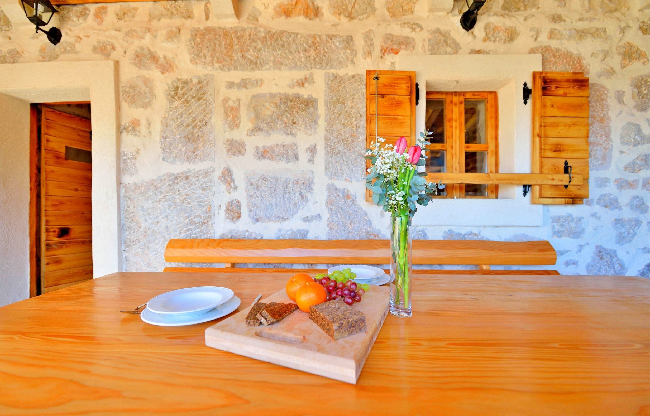 A wooden table with a cutting board, plates, and food items. A vase with flowers is on the table.