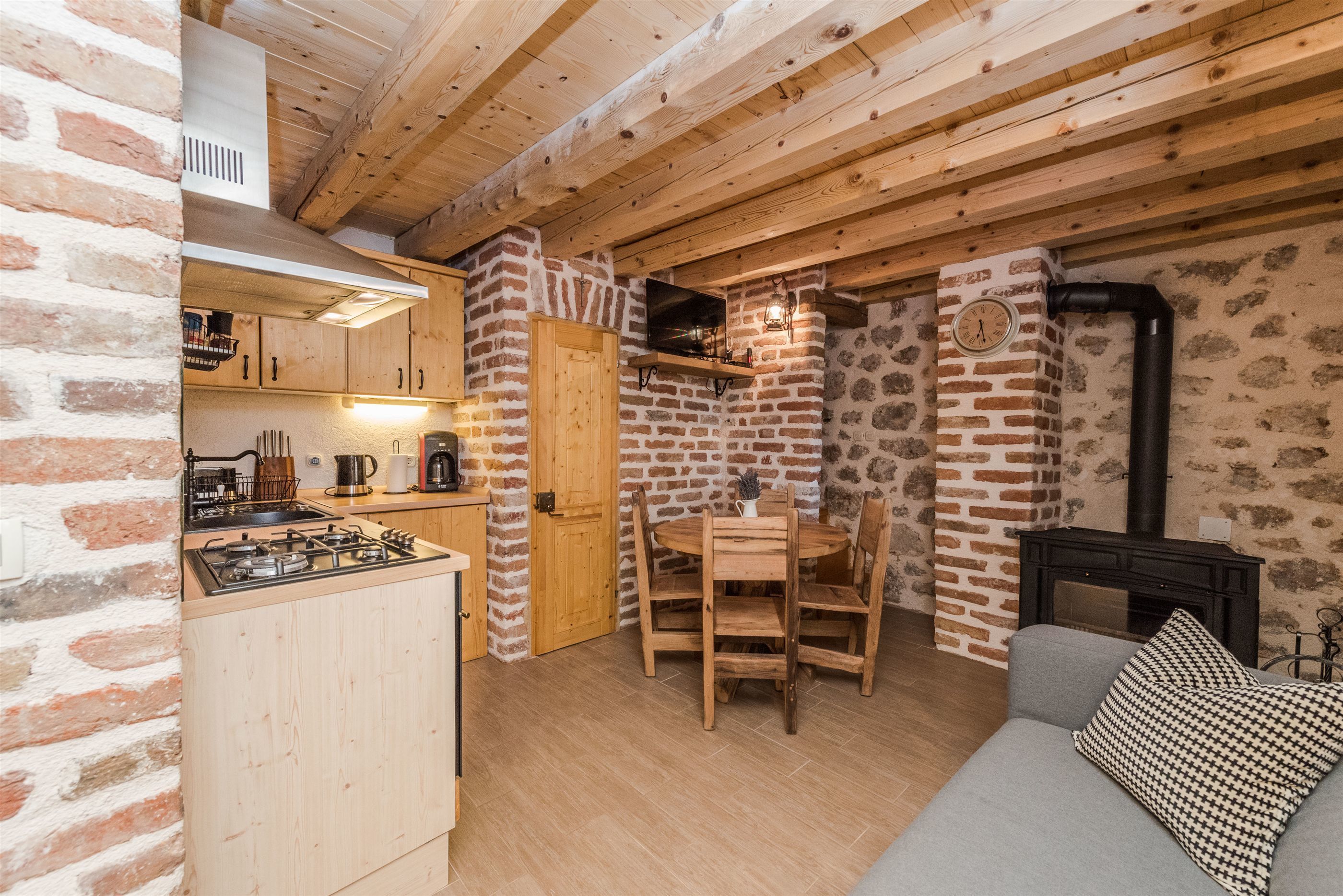 A rustic kitchen with wooden cabinets, a gas stove, and a brick wall.