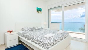 Una camera da letto con un letto, un comodino, un tappeto blu, un quadro e un'ampia finestra vista mare.