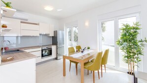 Una cucina moderna con mobili bianchi, un tavolo da pranzo con sedie e un'ampia finestra che fa entrare molta luce naturale.
