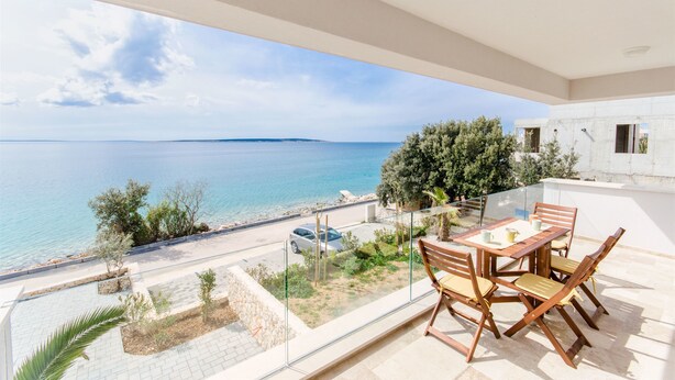 Un balcone con vista sul mare, un tavolo con sedie e una ringhiera in vetro.