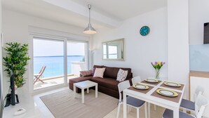 Un soggiorno moderno con divano, tavolino e tavolo da pranzo per quattro persone. Una grande finestra offre vista sul mare.