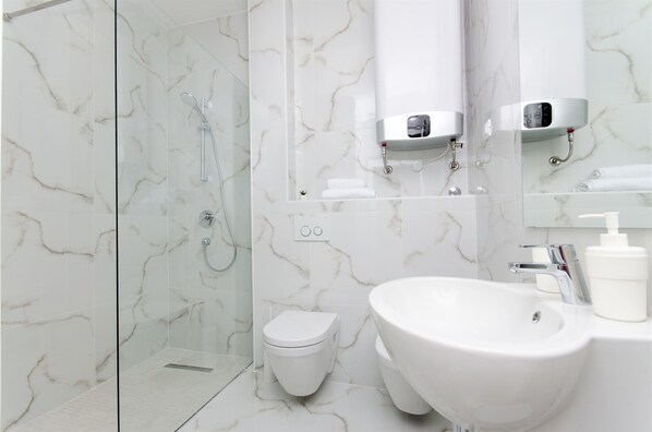 A modern bathroom with a glass shower enclosure, a white toilet, a large sink, and a mirror with a soap dispenser. - Apartments Branimir (Mandre)
