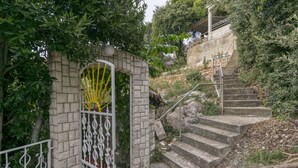 A stone staircase leading up to a building, surrounded by greenery and a metal gate with decorative elements. - Apartments Neno (Stanici)