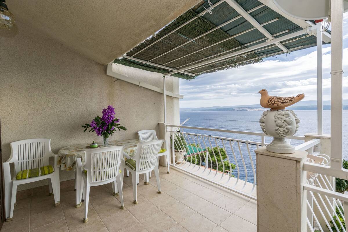 A balcony with white chairs, a table, a vase of purple flowers, and a decorative bird statue.