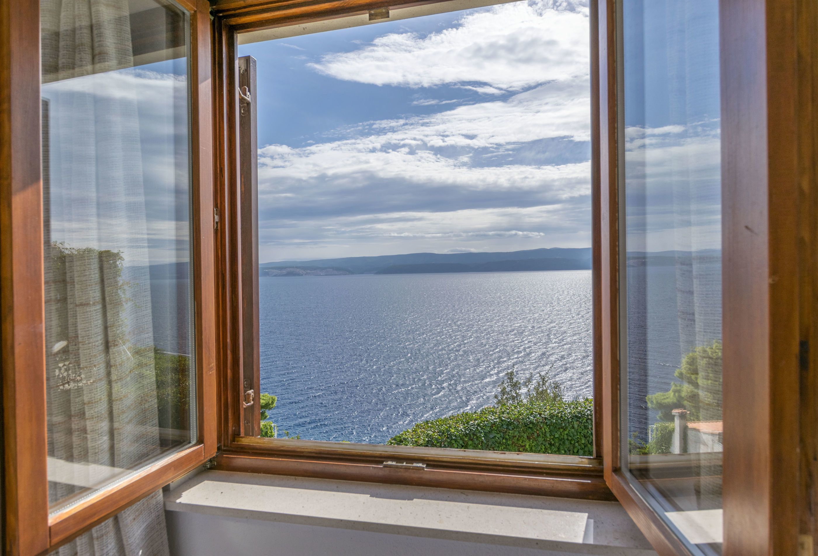 A window with a view of the sea and distant mountains.