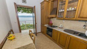 A kitchen with wooden cabinets, a gas stove, and a dining table with a fruit bowl. - Apartments Neno (Stanici)