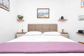 A neatly made bed with a pink blanket, a headboard, bedside lamps, and two framed artworks on the walls. - Apartments Neno (Omis)
