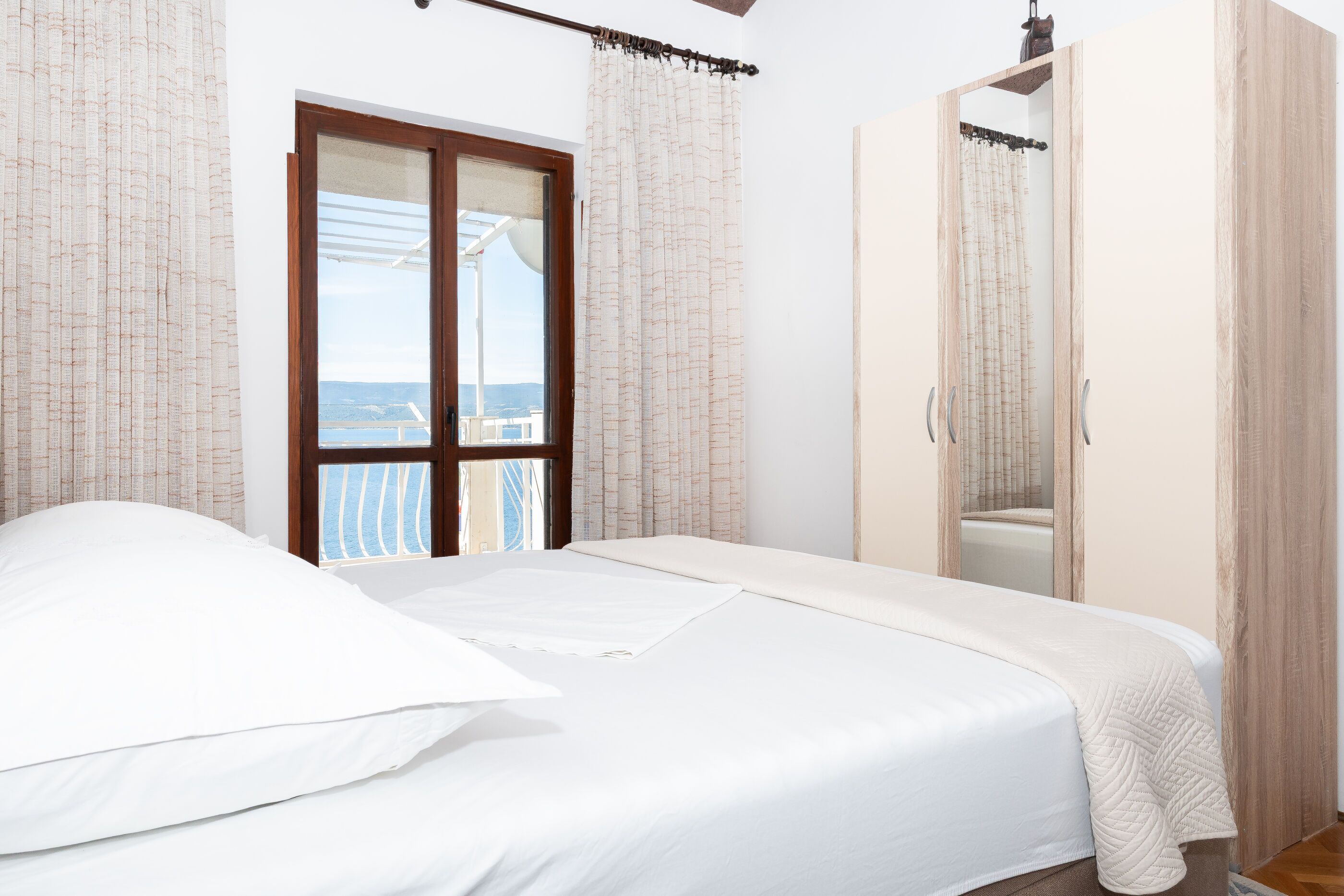 Une chambre à coucher avec un lit, une armoire et un balcon avec des rideaux.
