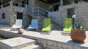 A stone building with a covered outdoor seating area, including white and green lounge chairs, a potted plant, and a staircase leading to an upper level. - House Romantica (Postira)