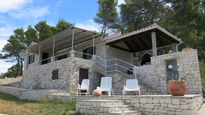 A stone building with a covered patio, outdoor seating, and a staircase leading to an upper level. - House Romantica (Postira)