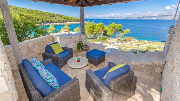 A covered outdoor seating area with wicker furniture and cushions, overlooking a scenic coastal view. - House Romantica (Postira)