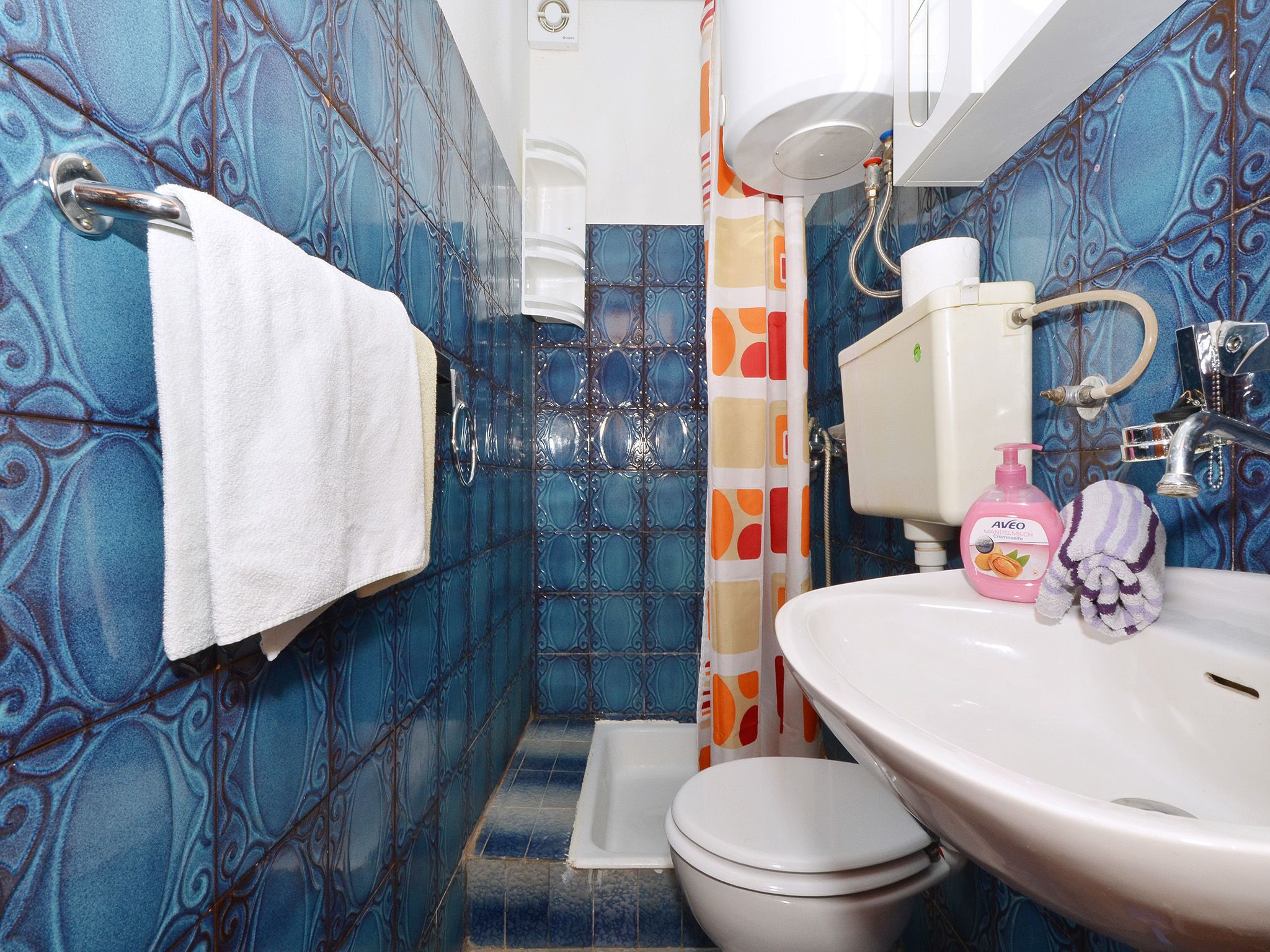 A bathroom with blue patterned tiles, a white sink, a toilet, and a shower curtain with a geometric pattern.