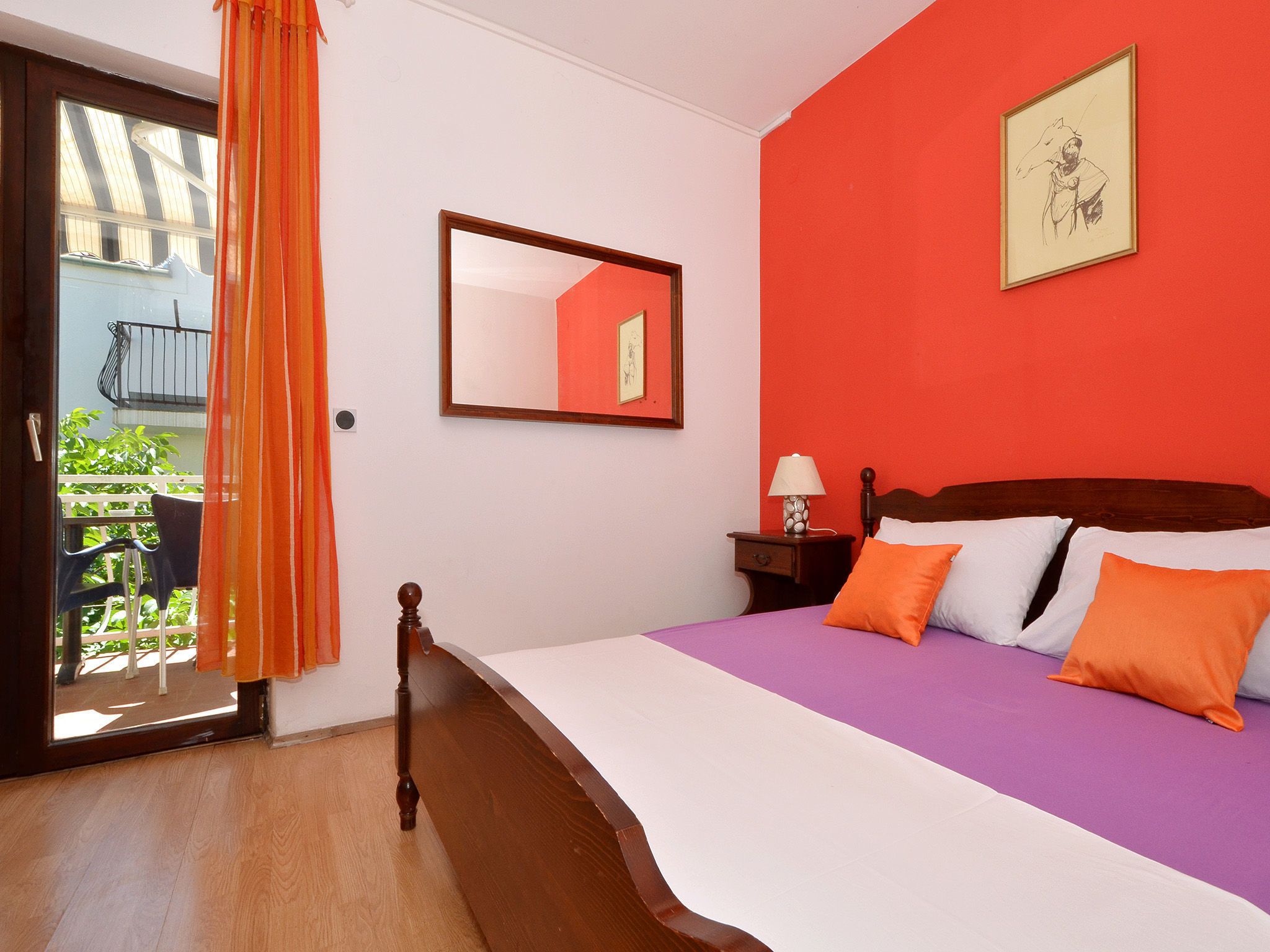 A bedroom with a bed, a nightstand, a lamp, a window with curtains, and a balcony.