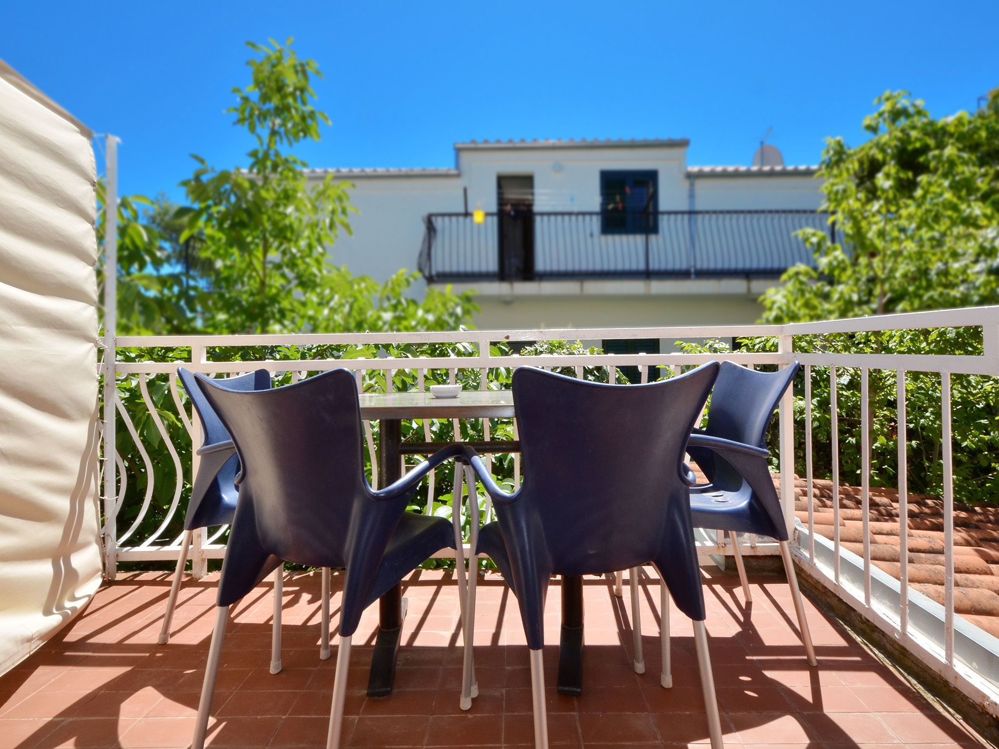 An outdoor terrace with a white railing, two blue chairs, and a table.