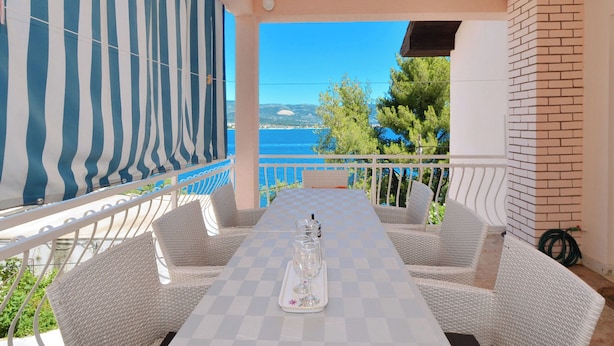 A terrace with a checkered table, wicker chairs, a striped awning, and a view of the sea.