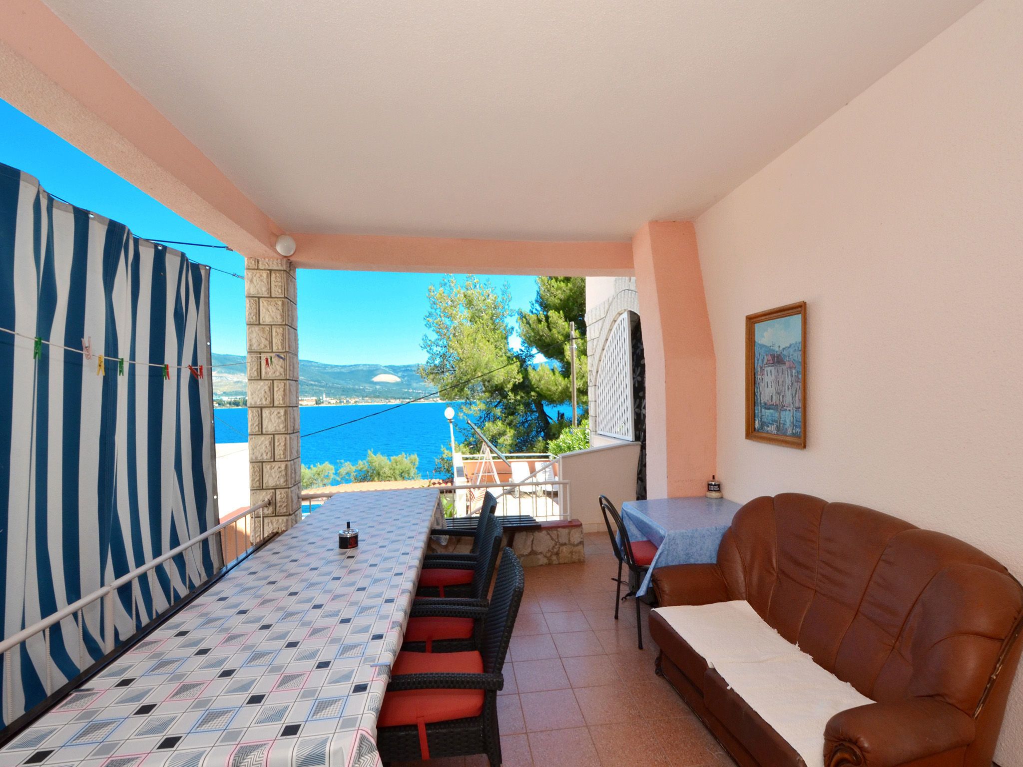 A room with a view of the sea, a patterned table, a brown leather sofa, and a painting on the wall.