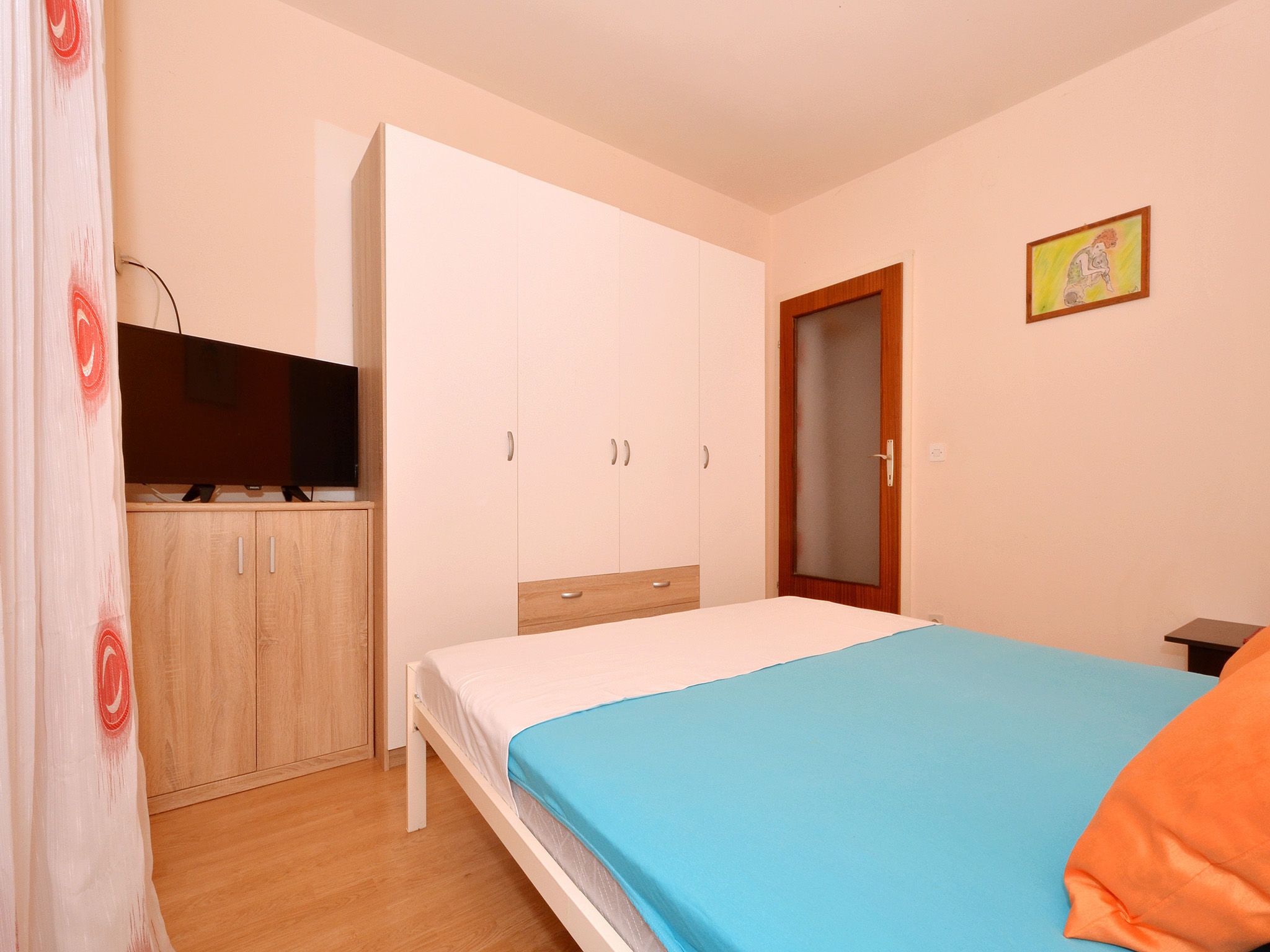 A bedroom with a bed, a wardrobe, a television, and a door.