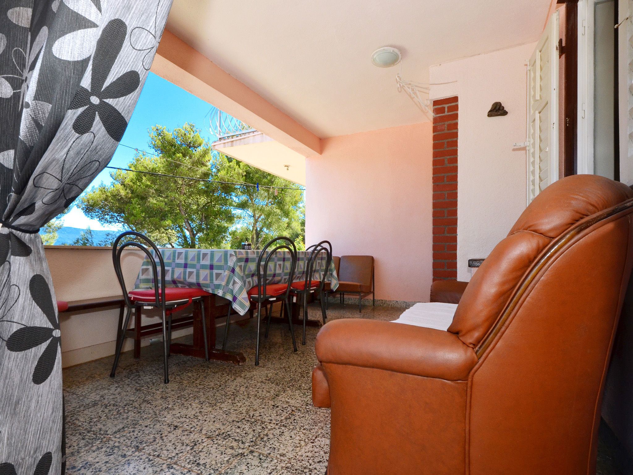 A balcony with a table and chairs, a leather chair, and a view of trees and a building.