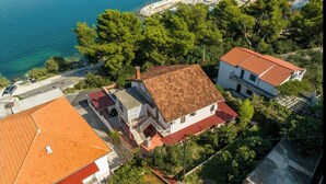 A coastal residential area with houses featuring red-tiled roofs and white walls, surrounded by greenery and a clear view of the sea.