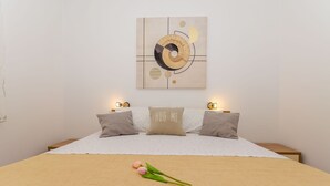 A neatly made bed with a beige blanket, two pillows, and a single rose on the bed. - Apartments Apollo (Zastrazisce)