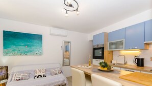 A modern kitchen with a dining area, a bed with a newspaper-themed pillow, and a painting of a seascape. - Apartments Apollo (Zastrazisce)