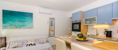 A modern kitchen with a dining area, a bed with a newspaper-themed pillow, and a painting of a seascape.