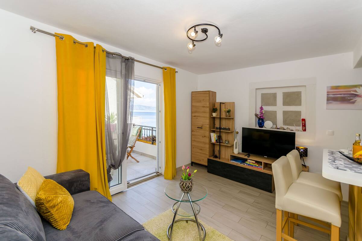 A modern living room with a sofa, a glass coffee table, a TV, and a dining area.