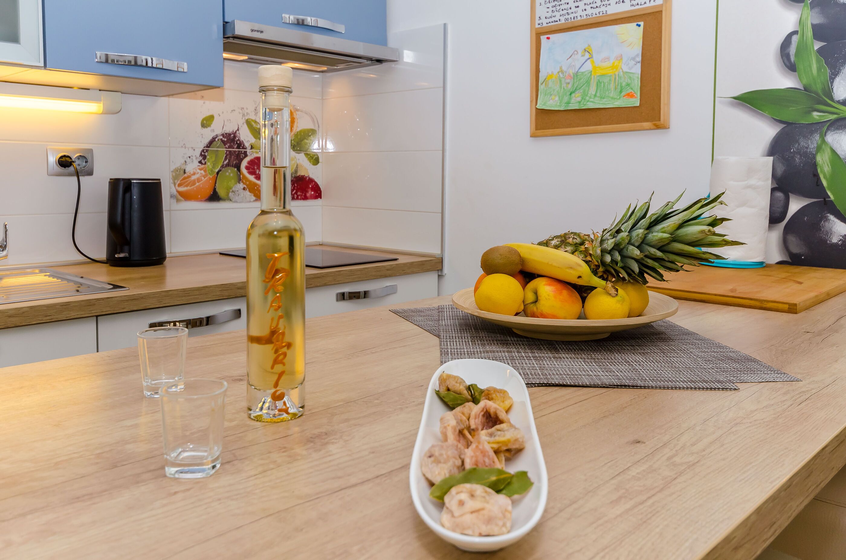 A kitchen with a wooden countertop, a bottle of olive oil, a plate of fruits, and a cutting board.