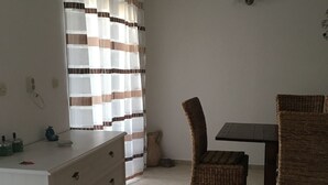 A room with a dining table, two wicker chairs, a white dresser with drawers, a striped curtain, and a tiled floor. - House Kupina (Gdinj)